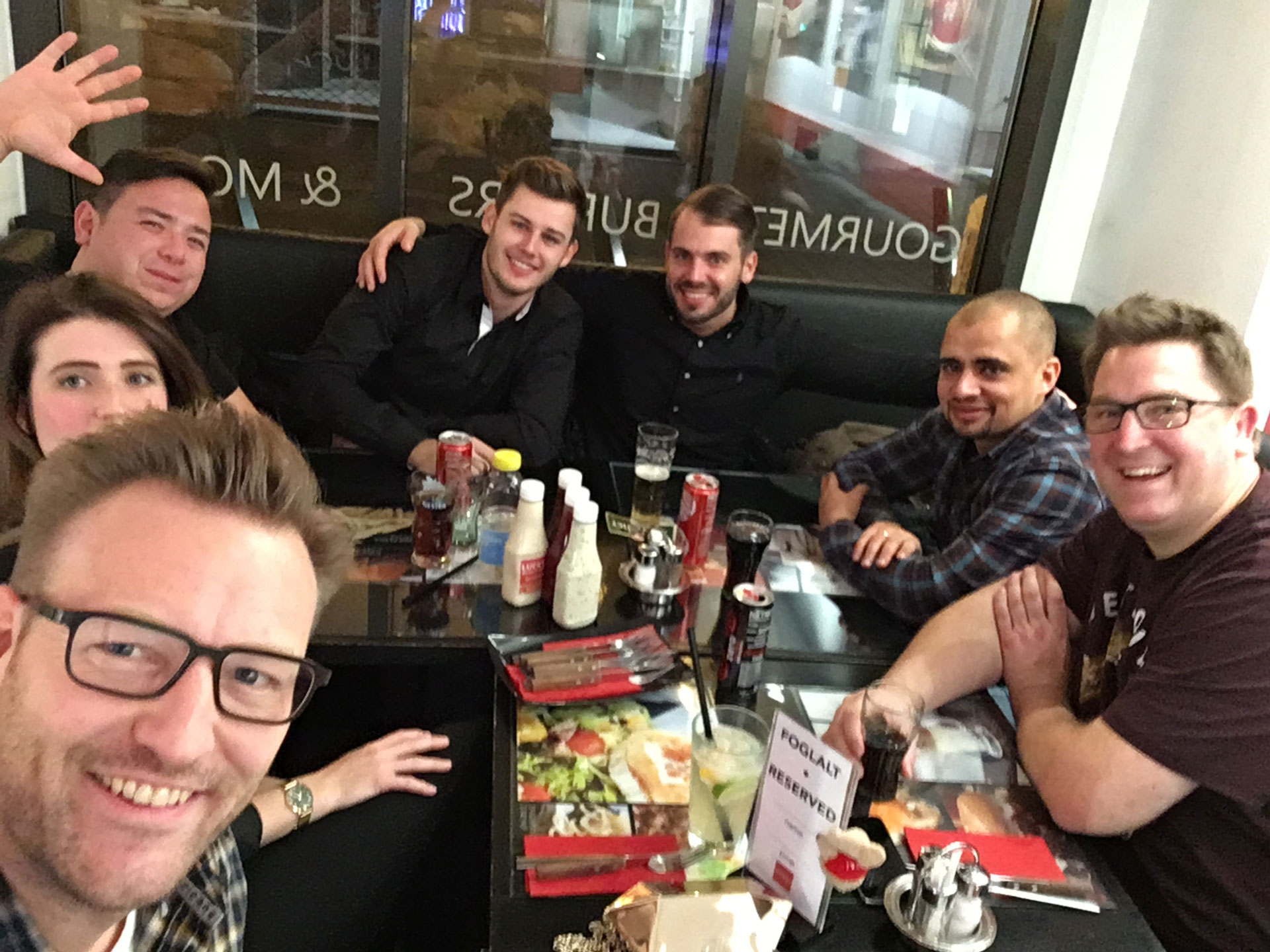 Foto: Gruppe junger Leute sitzt gemeinsam an einem gedeckten Restauranttisch, lacht und genießt Getränke und gute Stimmung.