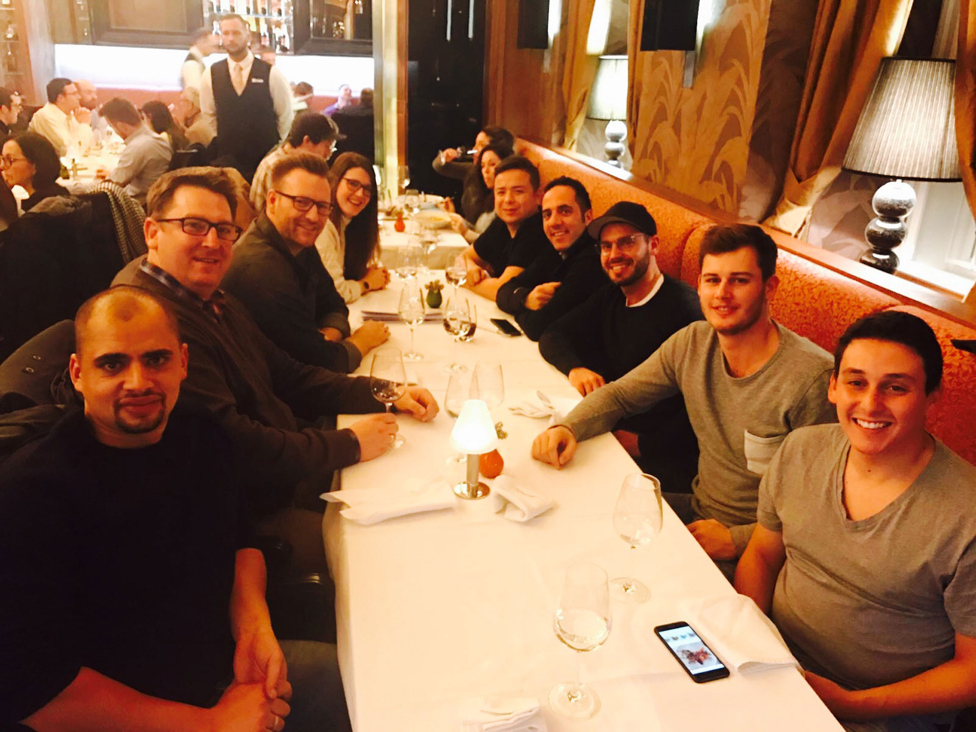 Foto: Zehn Personen sitzen an einer langen, festlich gedeckten Tafel in einem belebten Restaurant und genießen den Abend.