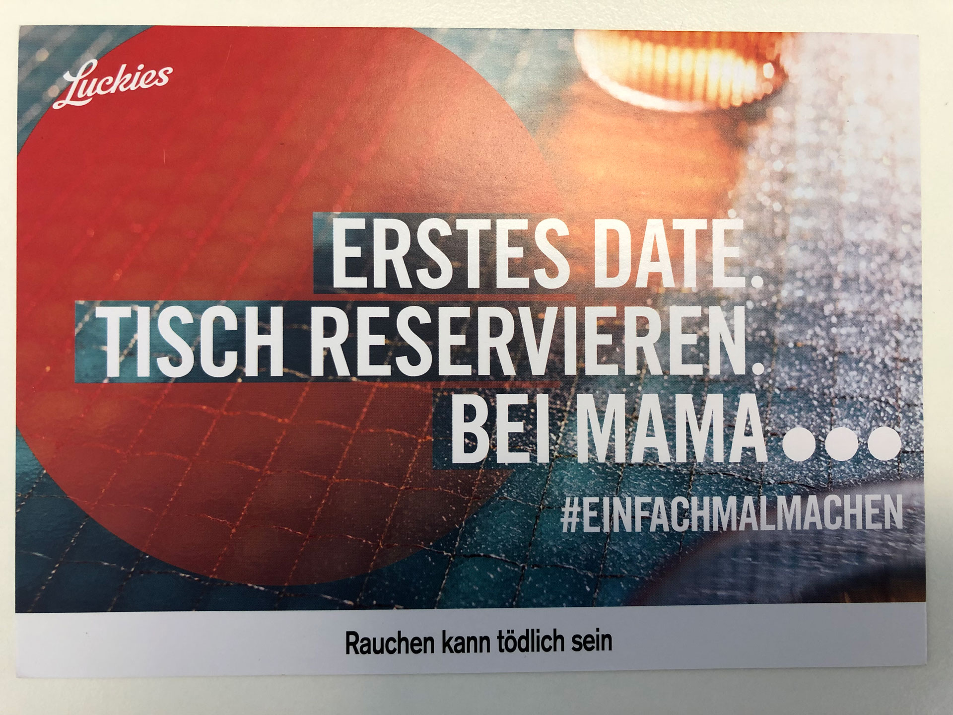 Foto: Postkarte mit Text „Erstes Date: Tisch reservieren. Bei Mama… #einfachmalmachen“ – darunter der Hinweis „Rauchen kann tödlich sein“.