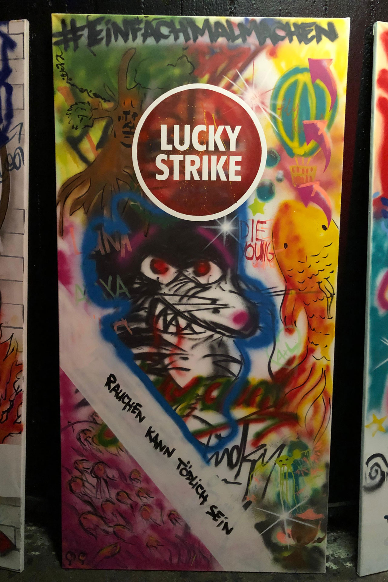 Foto: Buntes Graffiti-Plakat mit „Lucky Strike“-Logo, dem Namen „Sophie“, vielen Blumen und dem Schriftzug „Rauchen kann tödlich sein“.