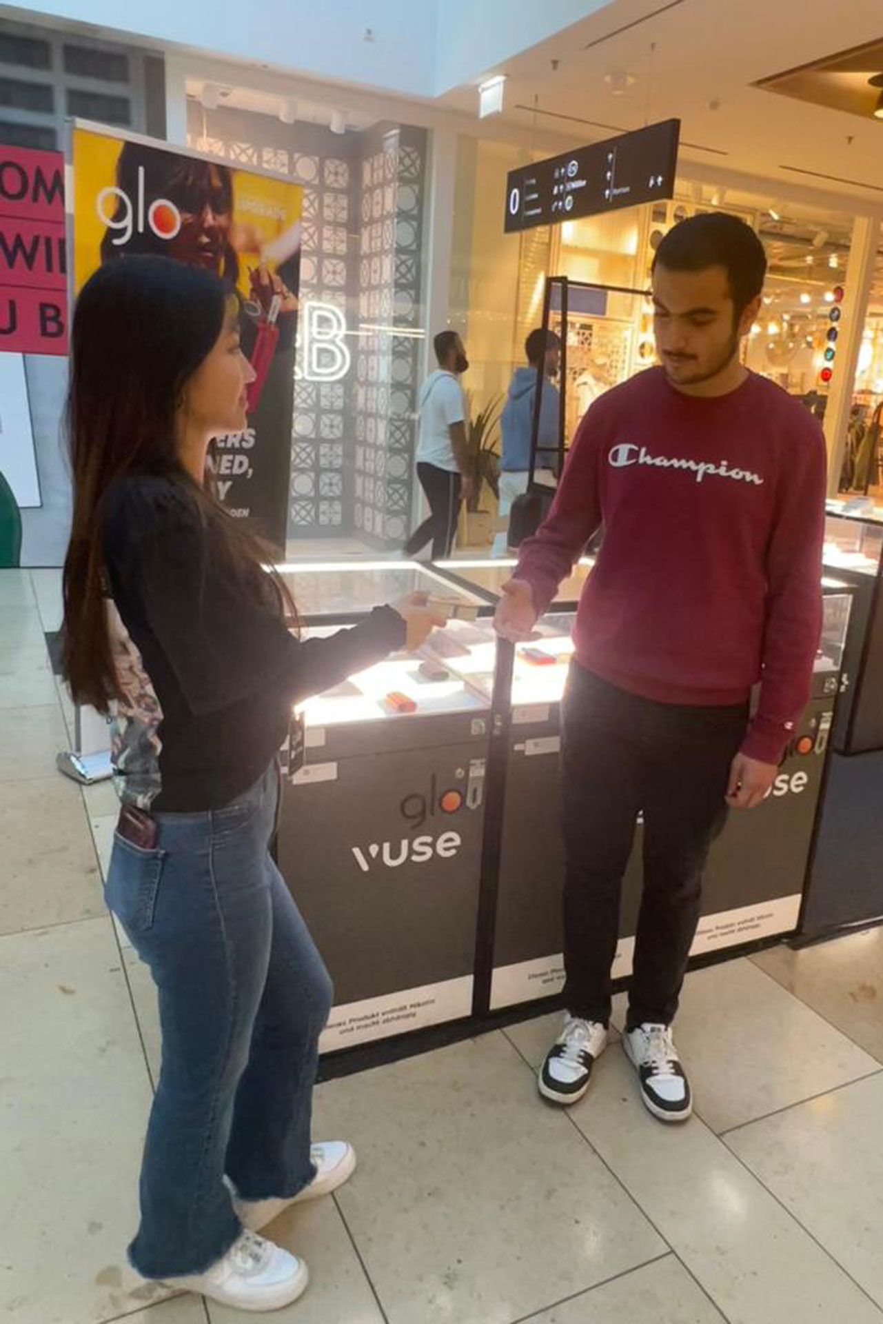 Foto: Promotion-Mitarbeiterin überreicht einem jungen Mann ein Vuse-Produkt in einem Einkaufszentrum.