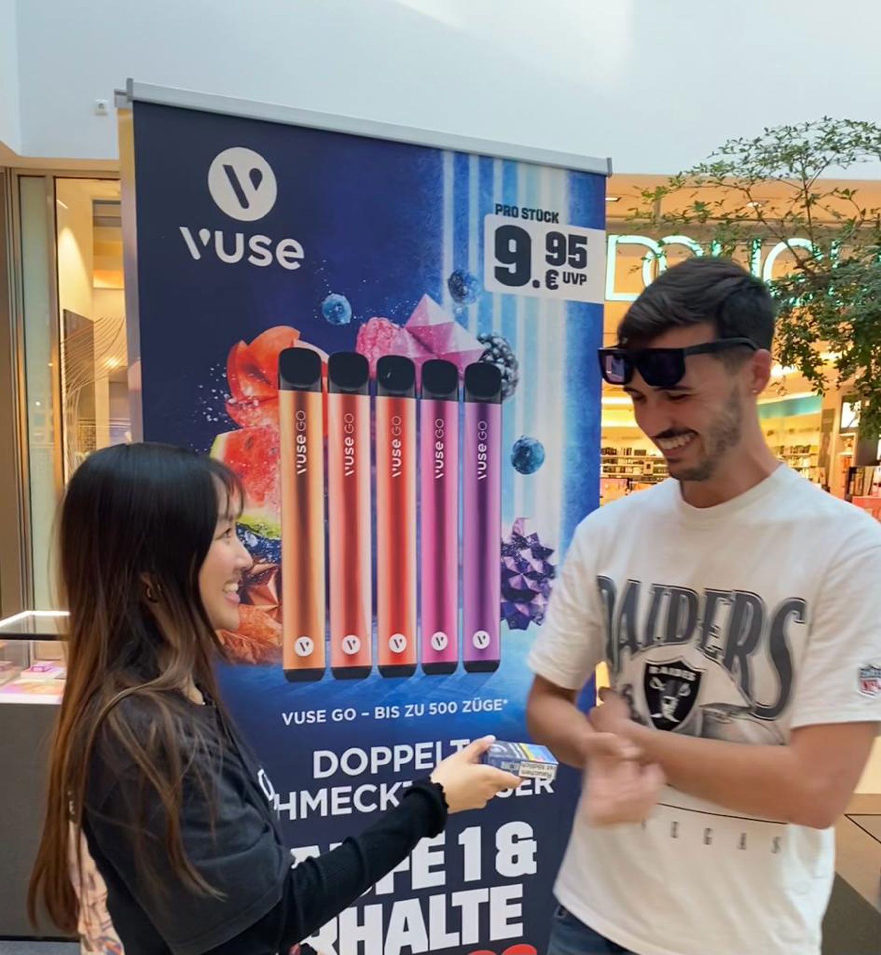 Foto: Promotion-Mitarbeiterin überreicht einem jungen Mann ein Vuse-Produkt in einem Einkaufszentrum.
